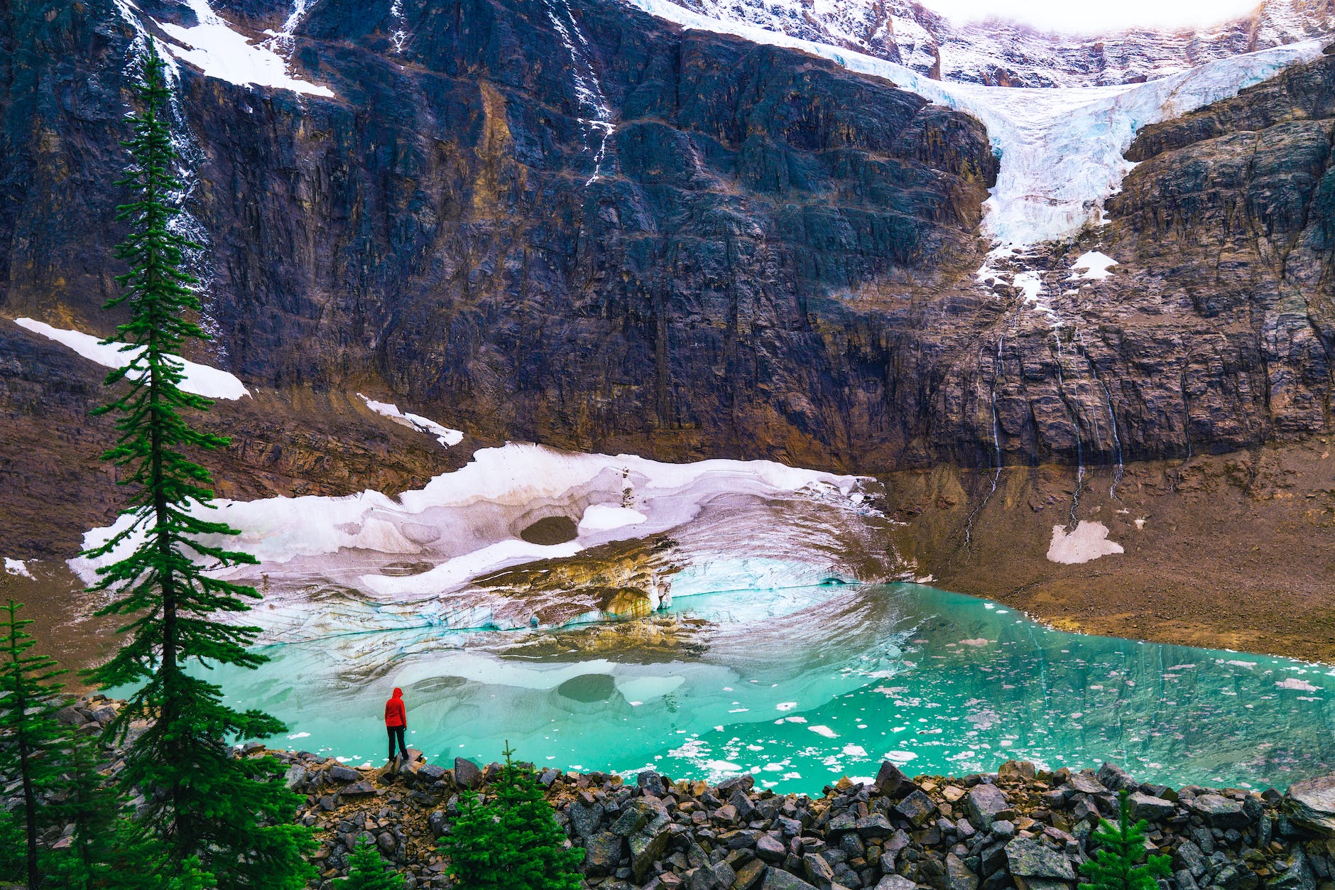 person in red shirt standing on rock near lake